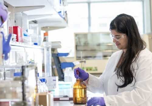 A member of the O'Reilly group at work in a lab, pipetting some liquid from a bottle